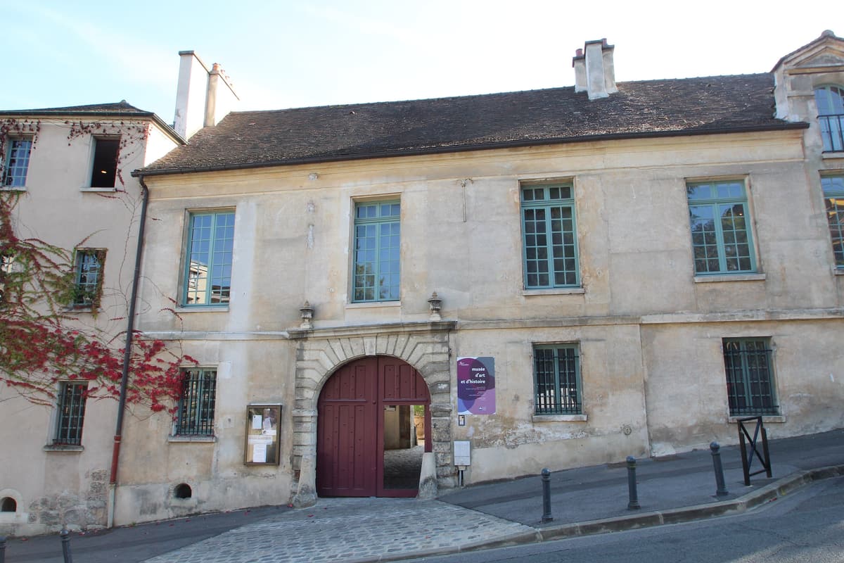 Façade ancienne à porche cintré et fenêtres à petits bois, le long d'une rue en pente.